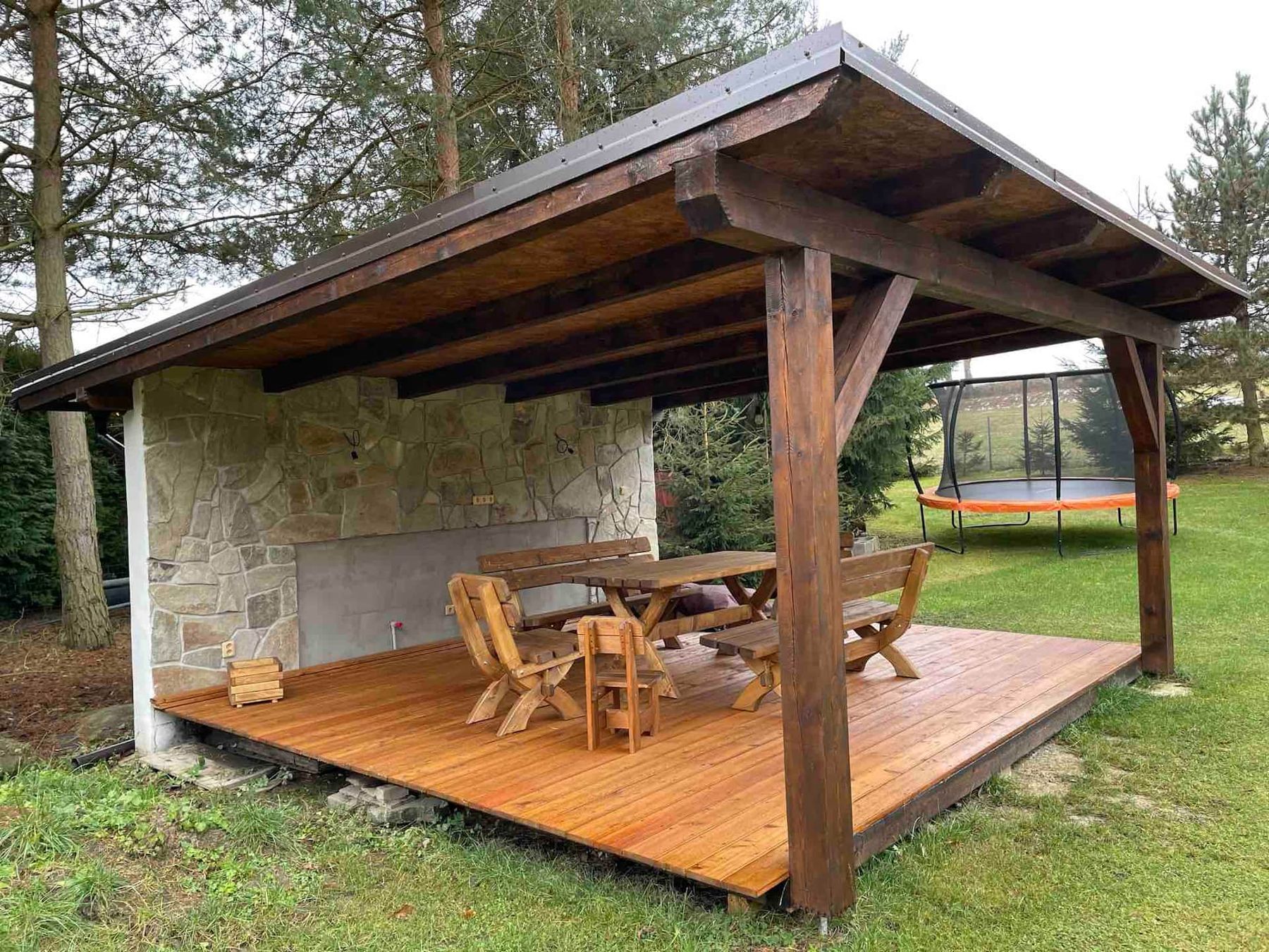 Velká dřevěná pergola s kamennou stěnou a stolem